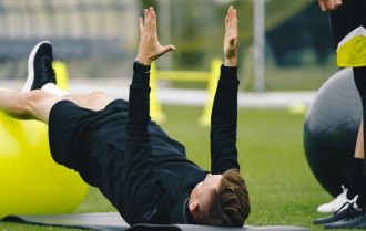 Young Coach Showing to Junior Players How to Exercise Properly on Training Mat and Training Yoga Ball